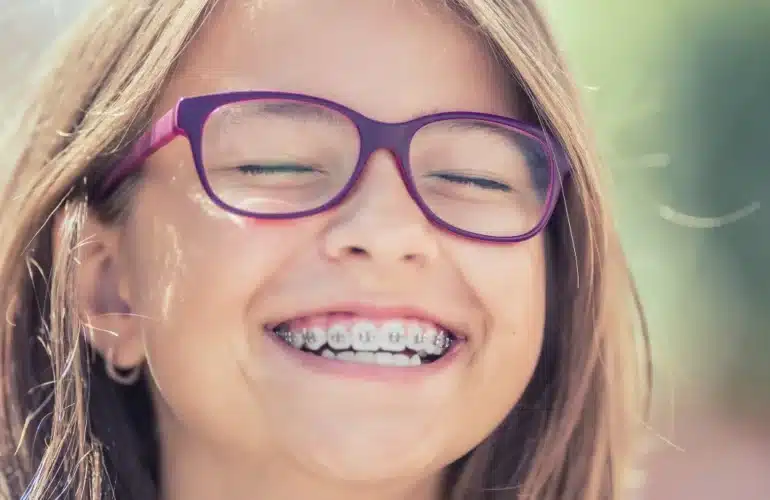 niña sonriendo en un dia soleado con gafas y brackets