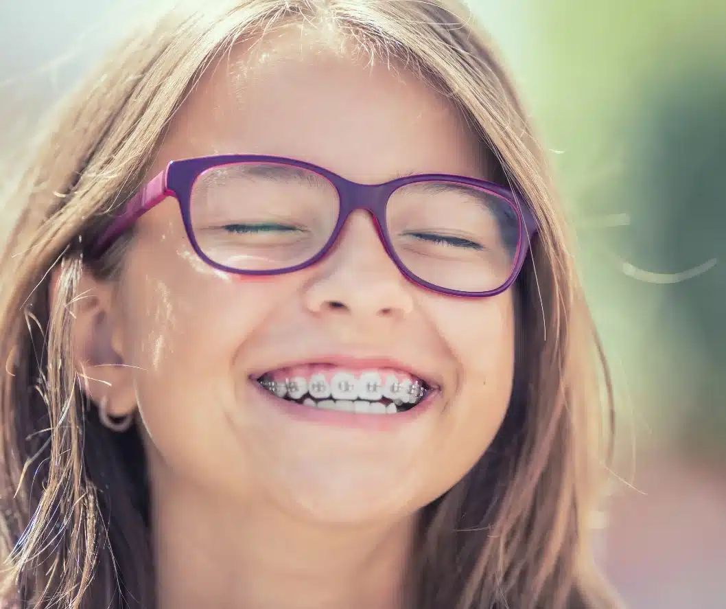 niña sonriendo en un dia soleado con gafas y brackets