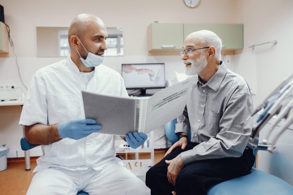 Dentista hablando con un paciente mayor en el consultorio, revisando juntos un historial médico dental.