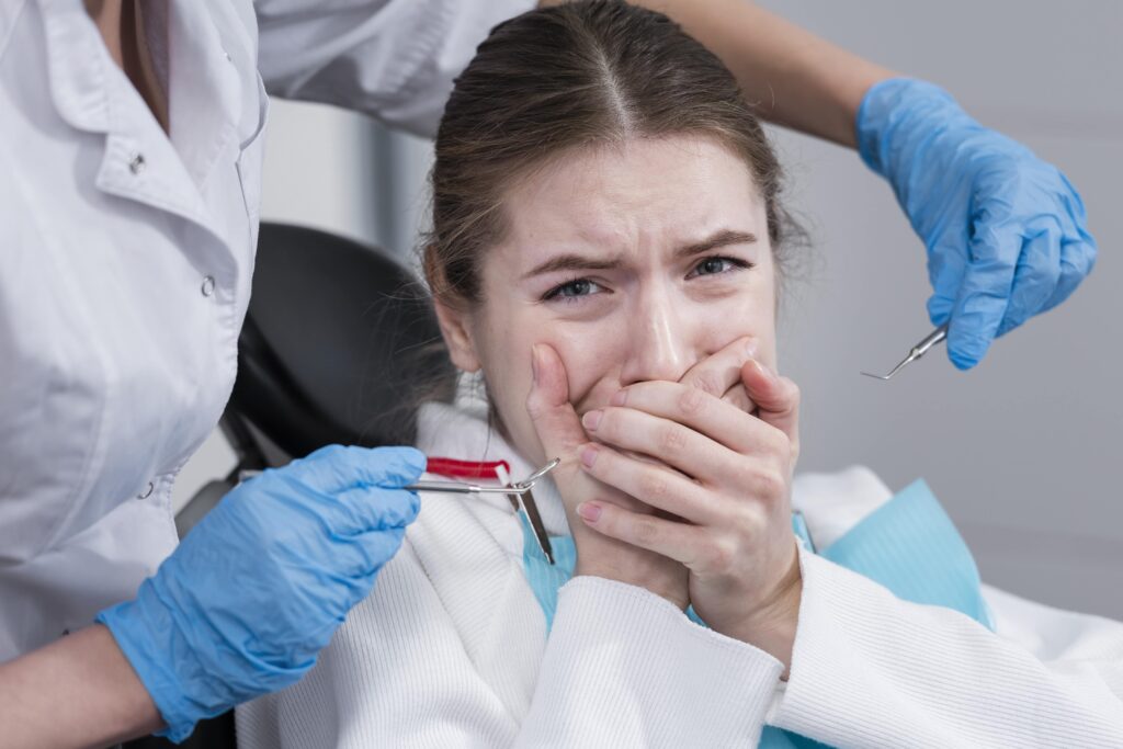 Mujer joven con expresión de miedo cubriéndose la boca mientras un dentista sostiene instrumentos odontológicos.