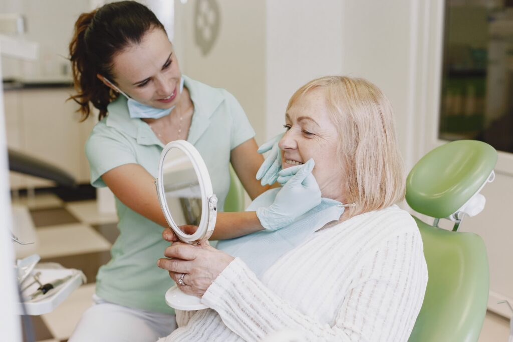 Dentista mostrando el resultado de un tratamiento dental a una mujer mayor que se observa en un espejo con una sonrisa satisfecha.