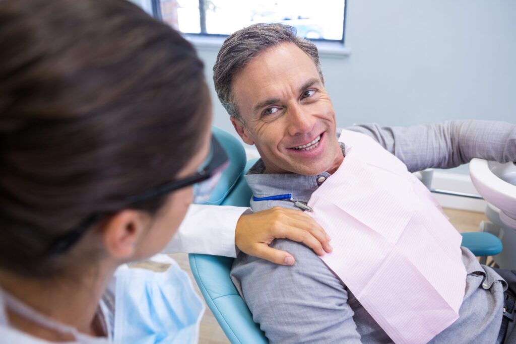 Hombre sonriente conversando con su dentista mientras está sentado en el sillón dental. 