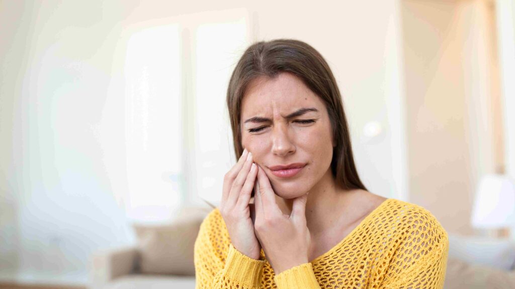 Chica con dolor de dientes, sosteniéndose la mejilla.