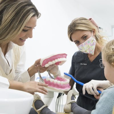 dentista infantil atendiendo un niño y enseñando como cepillar sus dientes